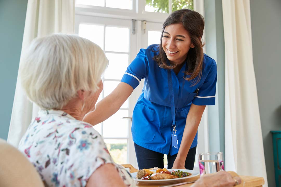 adult day care nurse serving dinner to a senior woman