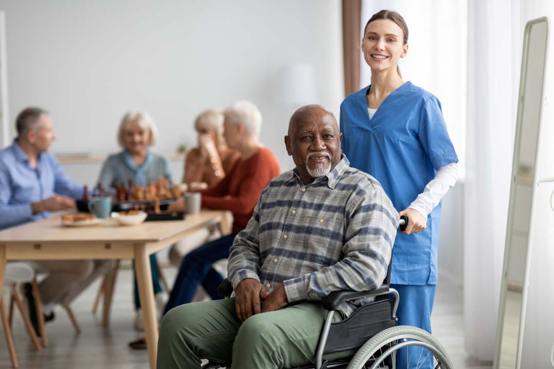 happy senior citizen in a wheelchair with smiling female nurse in adult daycare center