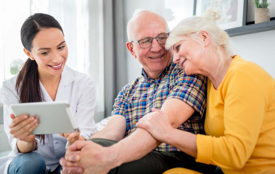 nurse showing smiling senior couple a tablet