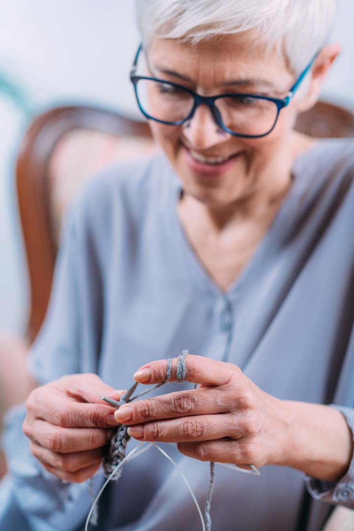 senior woman with glasses smiling and knitting
