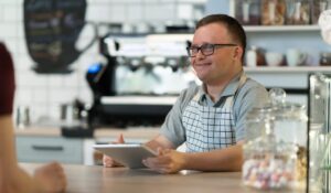 adult with special abilities smiling and taking a customers' order at a coffee shop